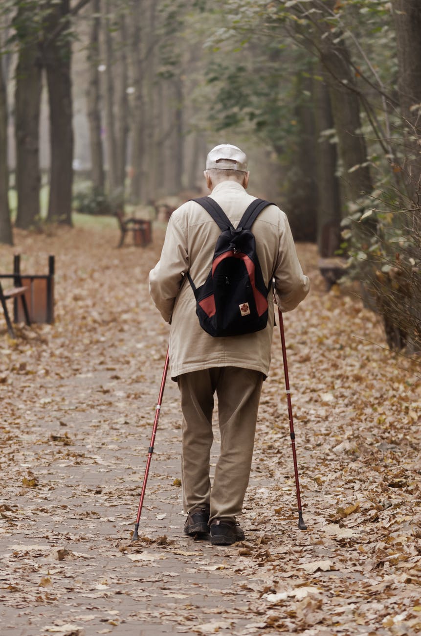 Older gentleman walking down path with walking sticks